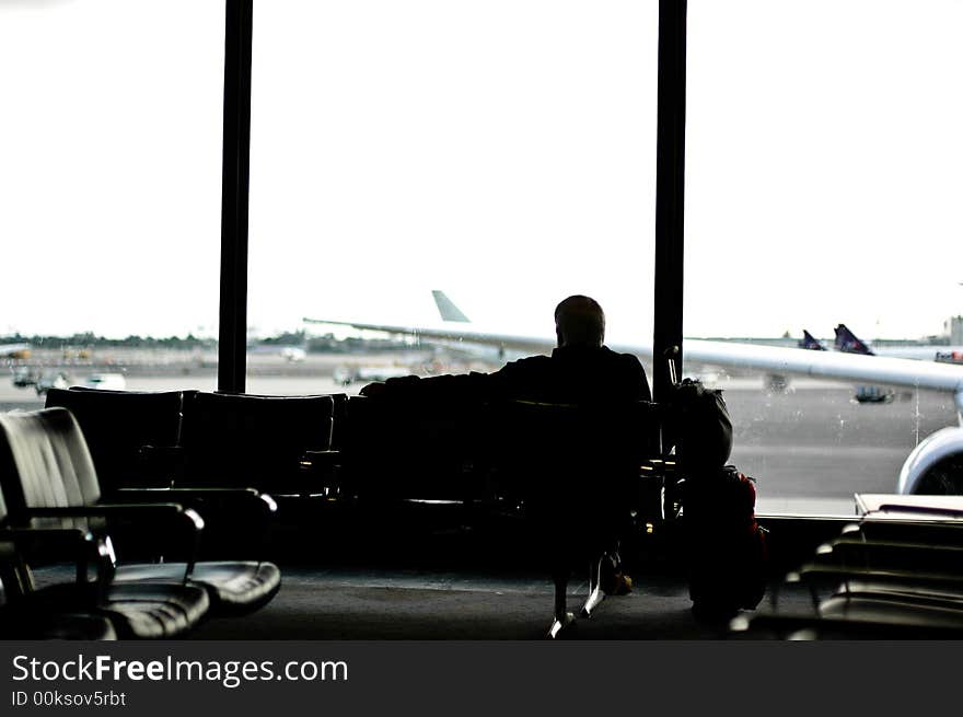 Man facing away from camera seated in airport lounge looking out the windows. planes visible through windows. Man facing away from camera seated in airport lounge looking out the windows. planes visible through windows.