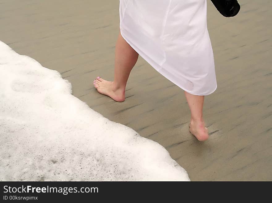 A lady on the beach walking by a wave. A lady on the beach walking by a wave