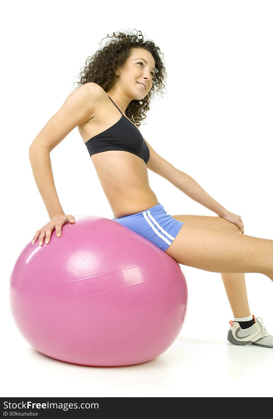 Young, beautiful woman sitting on big pink ball. Smiling and looking at something. White background, side view. Young, beautiful woman sitting on big pink ball. Smiling and looking at something. White background, side view