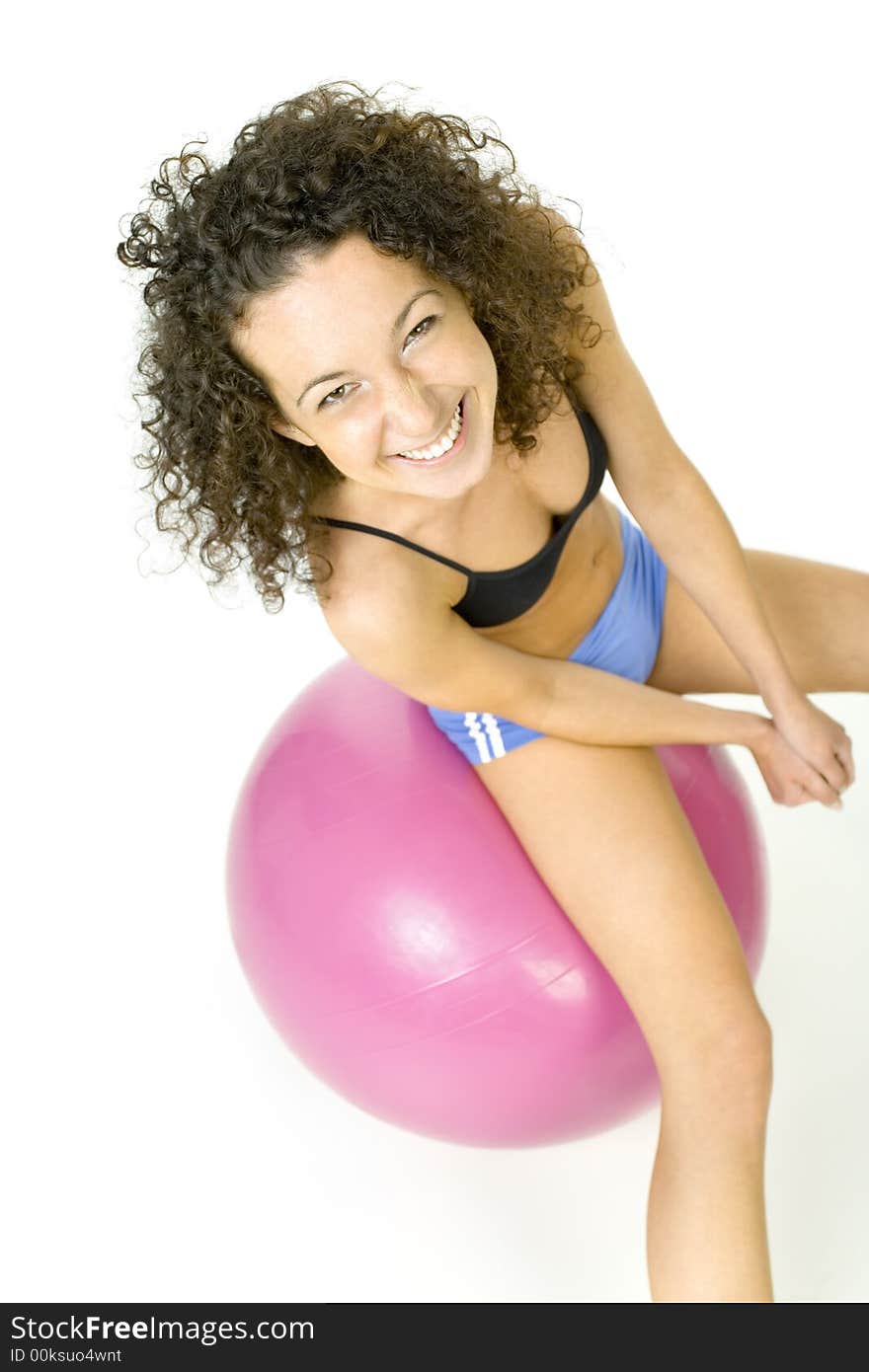 Young, beautiful woman sitting on big pink ball. Smiling and looking at camera. White background, high angle view. Young, beautiful woman sitting on big pink ball. Smiling and looking at camera. White background, high angle view