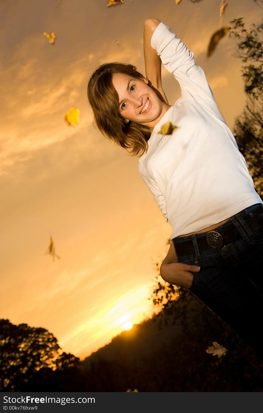 Beautiful young girl at sunset time and falling autumn leaves around her