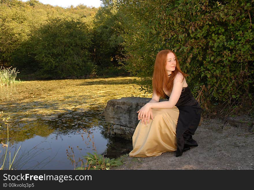 Auburn haired woman sits by lake. Auburn haired woman sits by lake.