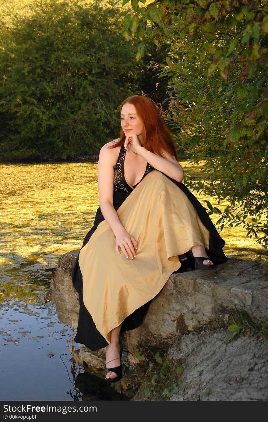 Auburn haired woman sits by lake. Auburn haired woman sits by lake.