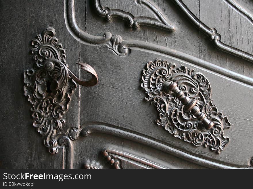 A detail of a large antique door handle and pull mounted in beautiful ironwork. A detail of a large antique door handle and pull mounted in beautiful ironwork.