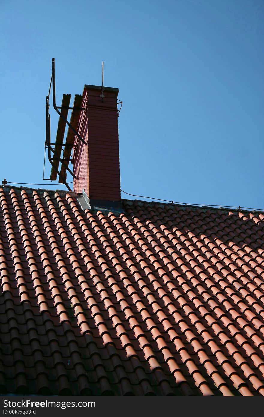 A chimney on top of a newly tiled roof on a bright summer day (deep shadows, red roof, blue sky).