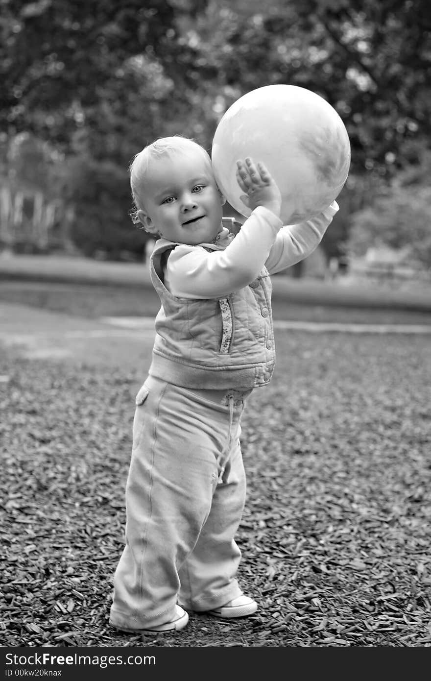 Black and white image of a small caucasian blond toddler holding an inflated rubber ball in a park setting. Black and white image of a small caucasian blond toddler holding an inflated rubber ball in a park setting