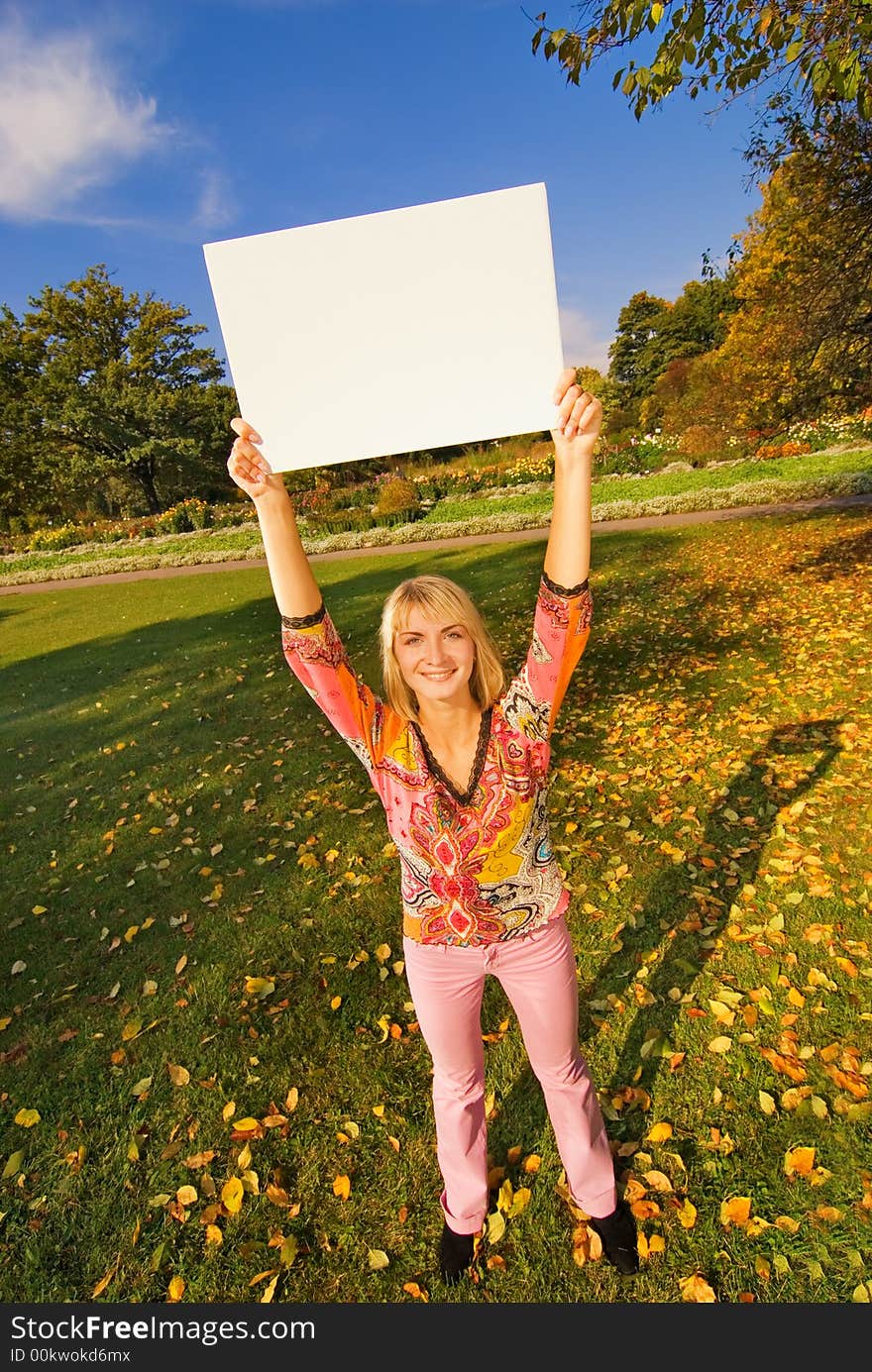 Beautiful girl on autumn background holding a white noticeboard