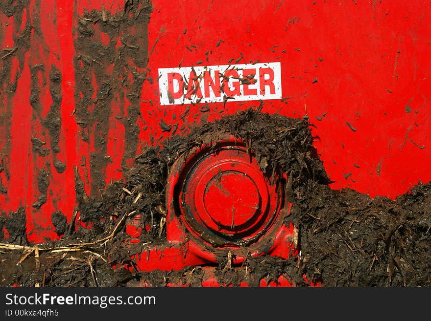 Danger sign splattered by muck on the back of a red muck spreader. Danger sign splattered by muck on the back of a red muck spreader