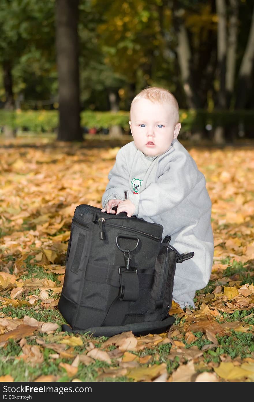 Little child stands on the yellow fallen foliage near to the big black bag. Little child stands on the yellow fallen foliage near to the big black bag