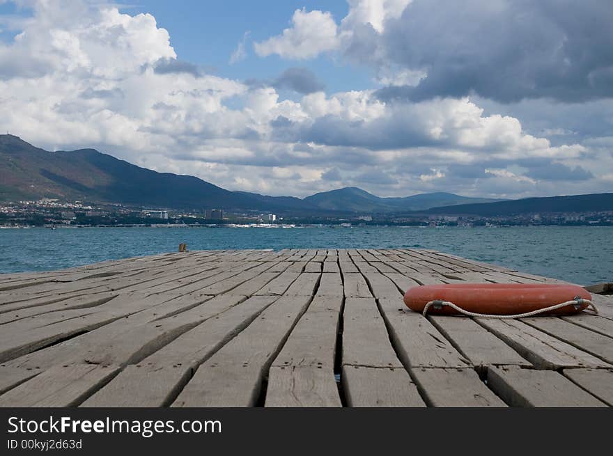 A wooden mooring with a life-buoy ring in seaside small town.