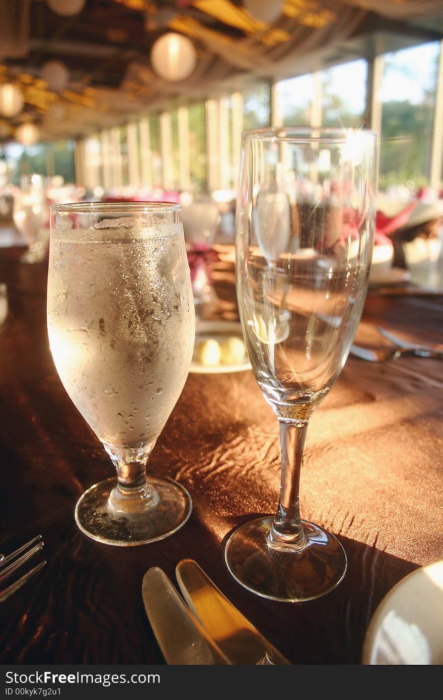 A water glass and a wine glass sitting on a table at a party. A water glass and a wine glass sitting on a table at a party.