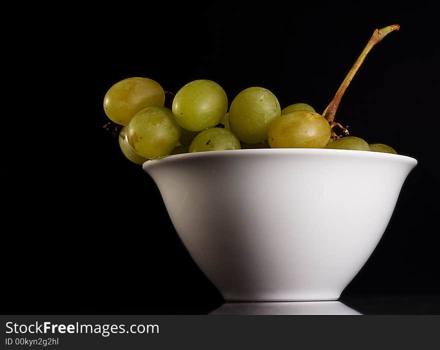 Withe grapes into a withe bowl against a black background