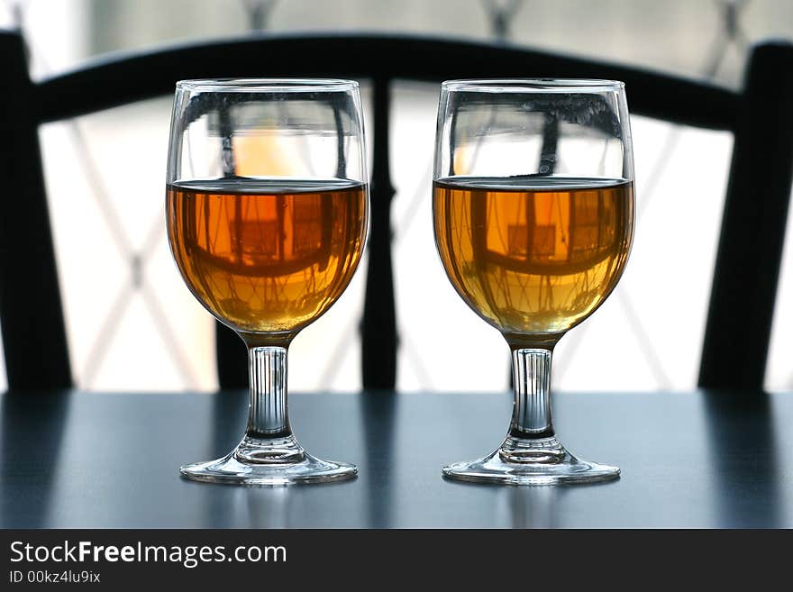 Two glasses of tea on a black table top with outdoor natural light behind