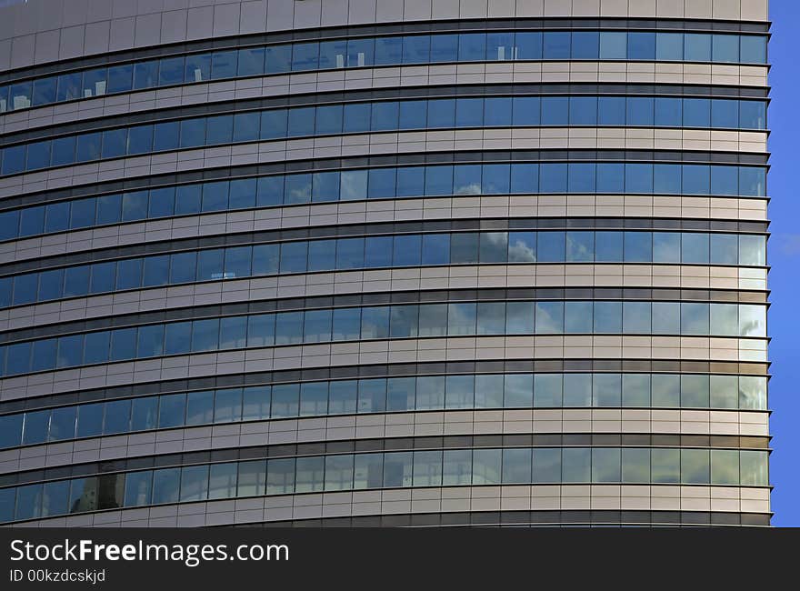 Modern  round tower skyline. Glass and metal on blue clear sky.Clouds reflexions. Modern  round tower skyline. Glass and metal on blue clear sky.Clouds reflexions.