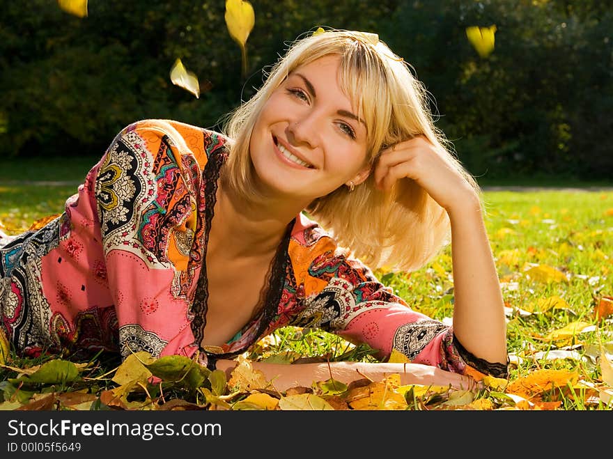 Blond cheerful girl lying on autumn leaves