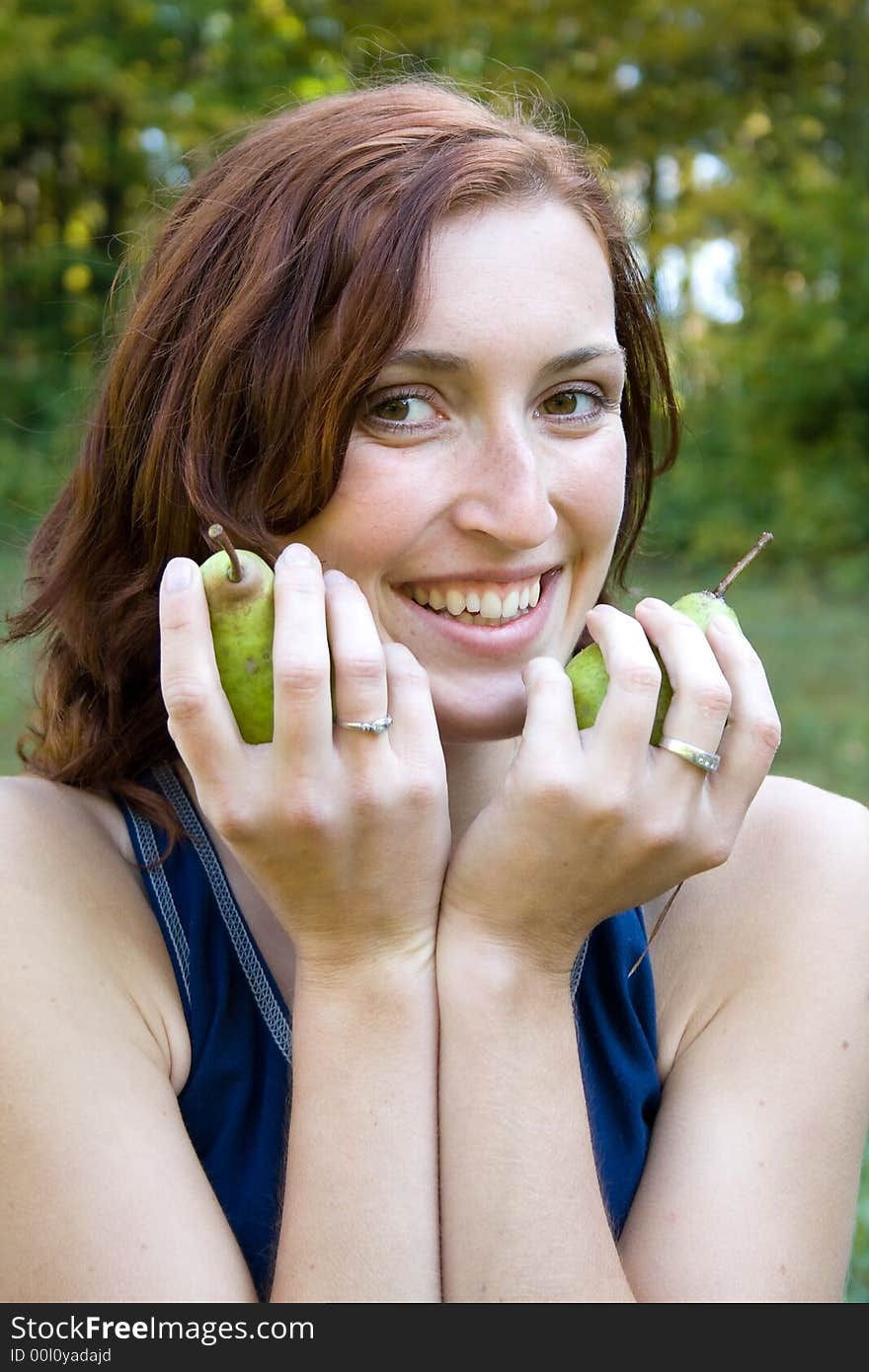 A smiling woman is holding pears in green nature