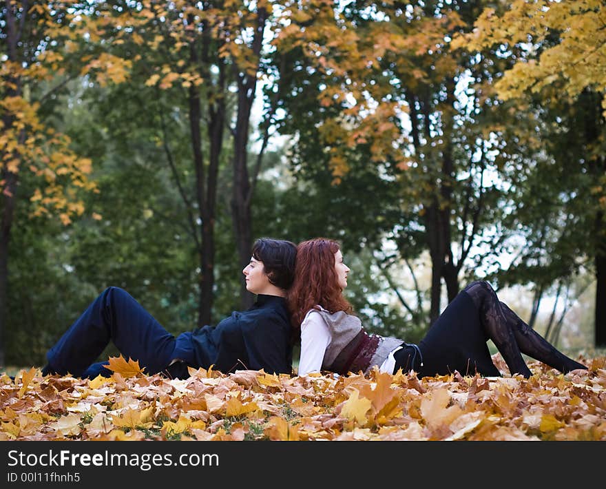 Two girls relaxing on maple leaves in park. Two girls relaxing on maple leaves in park