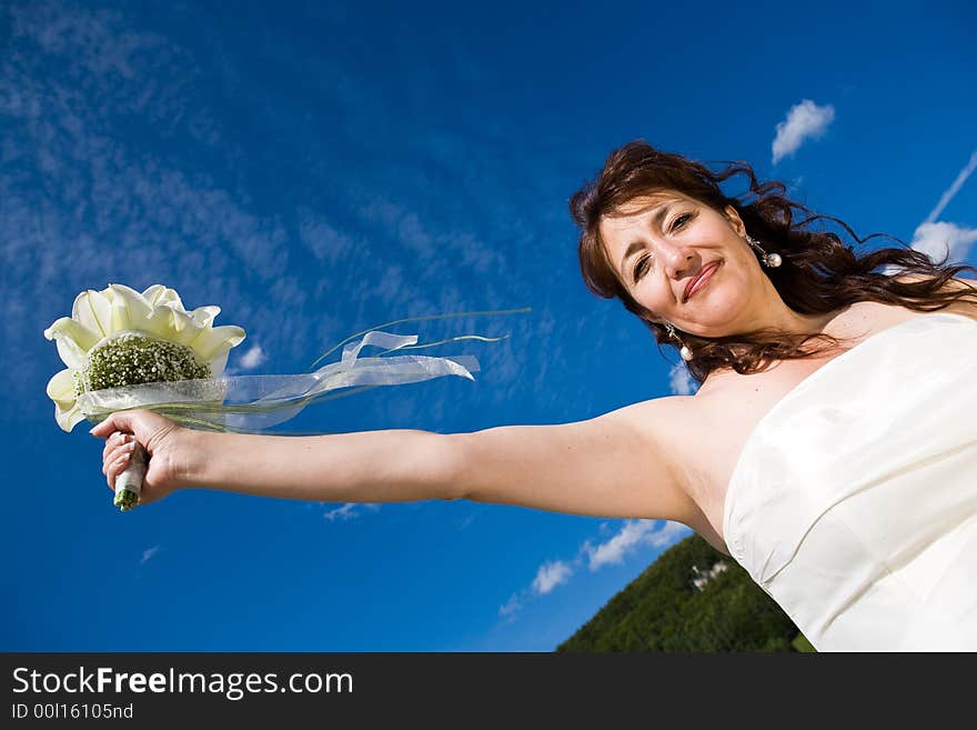 Fancy Perspective. Bride holds her bridal bouquet on outstretched arm. Deepblue sky as background. Sunny weather. Adult bride. Fancy Perspective. Bride holds her bridal bouquet on outstretched arm. Deepblue sky as background. Sunny weather. Adult bride.