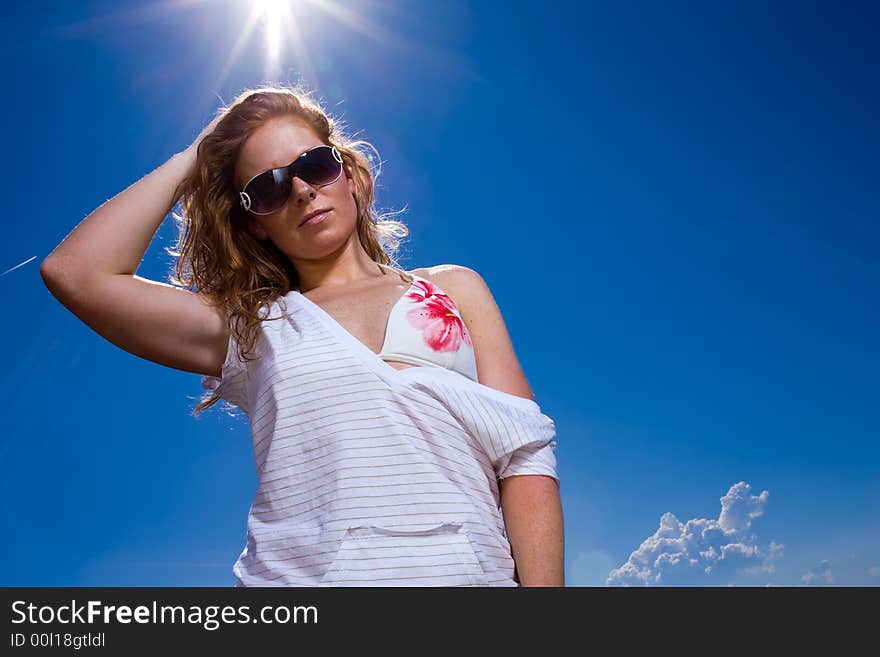 Attractive redhaired woman with freckles. Looking cool with big sunglasses, casual wear and bikini into camera. Deep blue sky with Lensflares. Attractive redhaired woman with freckles. Looking cool with big sunglasses, casual wear and bikini into camera. Deep blue sky with Lensflares