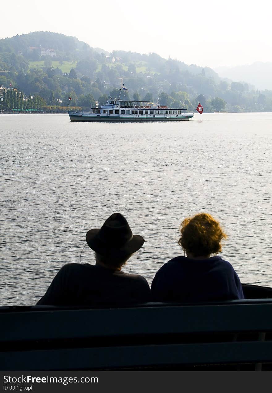 Couple sitting on a bench in switzerland watching a ship passing by. Couple sitting on a bench in switzerland watching a ship passing by