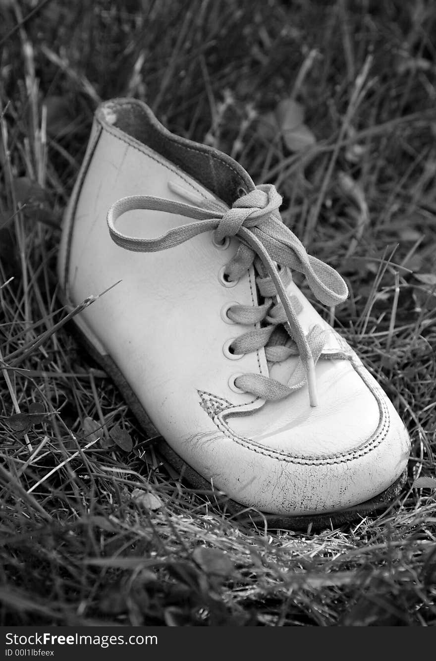 Old white baby boots on grass.