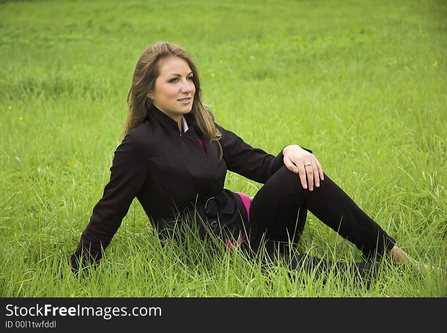 The beautiful girl sits on a green grass. The beautiful girl sits on a green grass