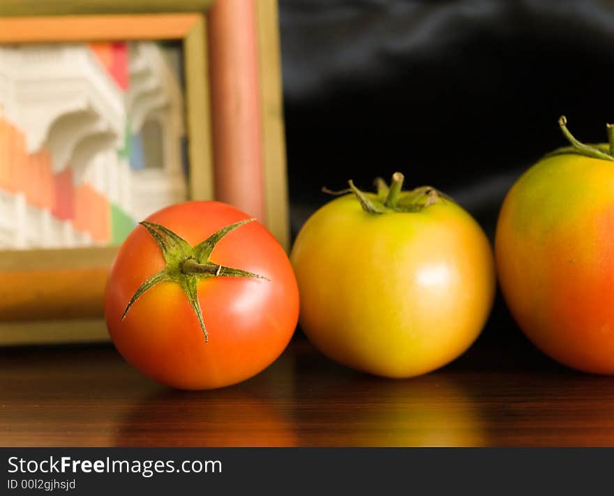 Still life of a row of tomatoes of increasing sizes against a framed picture on a black back drop. Still life of a row of tomatoes of increasing sizes against a framed picture on a black back drop