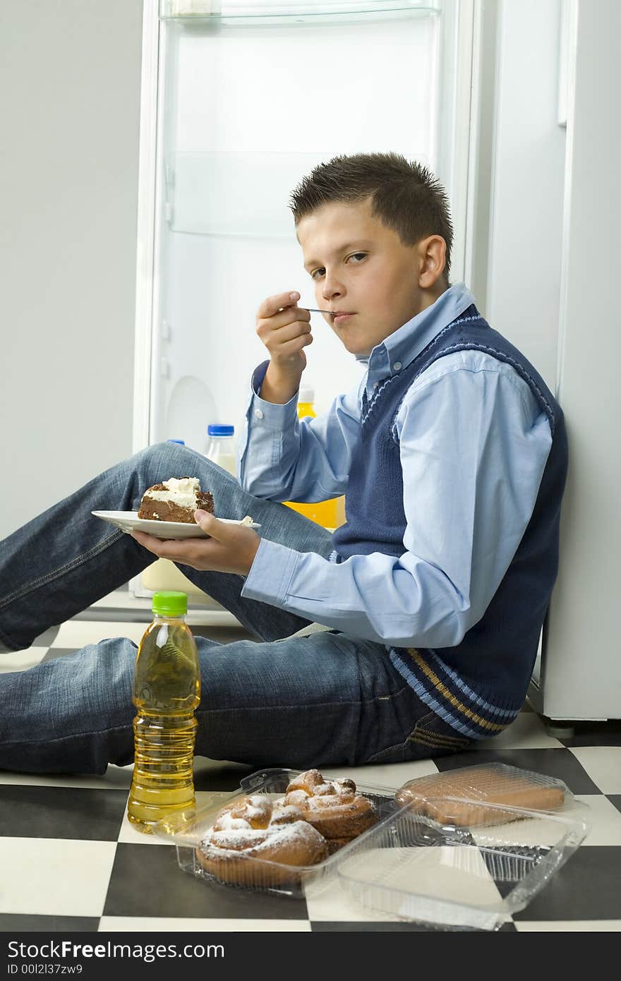 Boy sitting on the floor and eating cake. Side view. Looking at camera. Boy sitting on the floor and eating cake. Side view. Looking at camera.