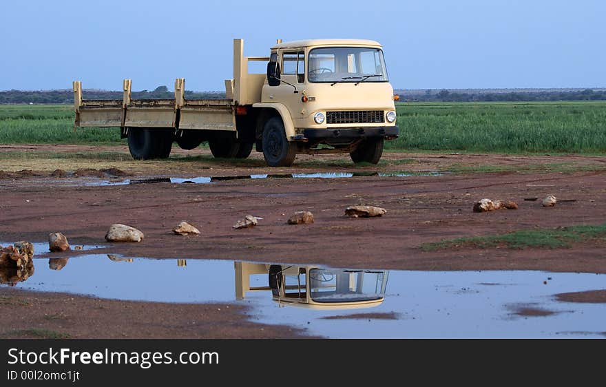 An old farm truck next to a field. There are some puddles left by recent rain with the reflection of the truck on them. An old farm truck next to a field. There are some puddles left by recent rain with the reflection of the truck on them.