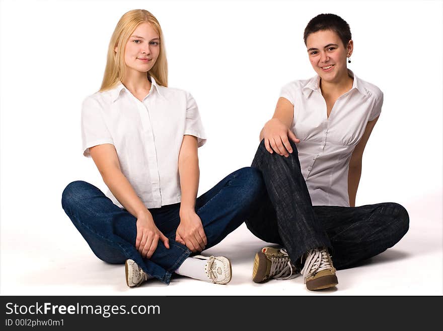 Two young girls blonde and brunette sits on the floor on white background