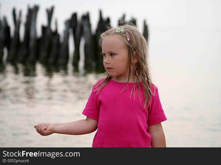 A girl holding a stone in her hand in front of old abandoned bridge in Sventoji (Lithuania) on the coast of the Baltic sea. A girl holding a stone in her hand in front of old abandoned bridge in Sventoji (Lithuania) on the coast of the Baltic sea