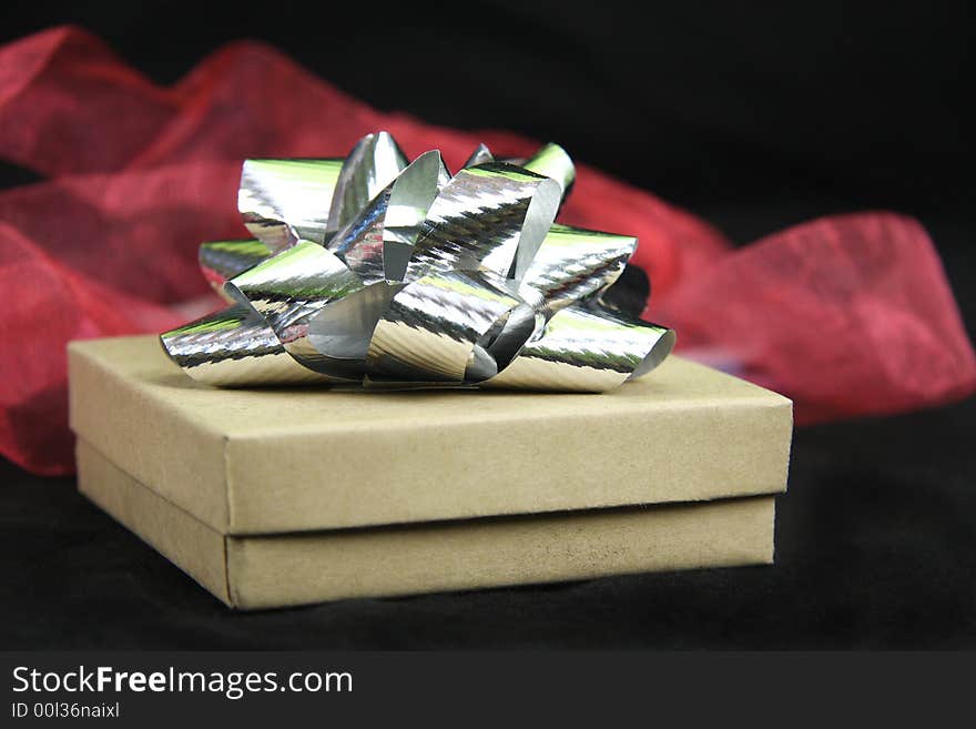 Gift box with silver bow on top with black background and red fabric behind