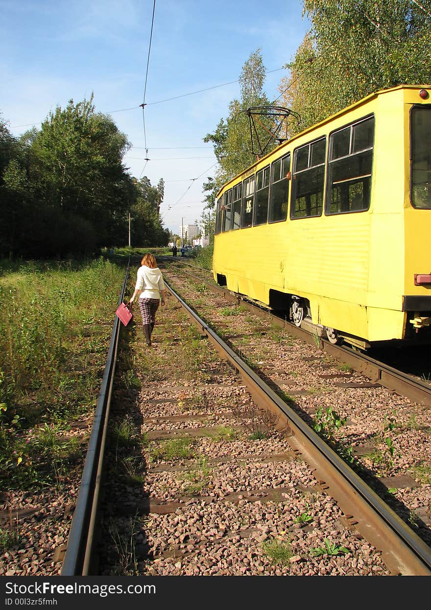 The young girl goes near to yellow tram