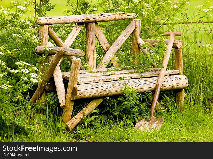 A wooden seat and wooden shovel in a garden setting. A wooden seat and wooden shovel in a garden setting