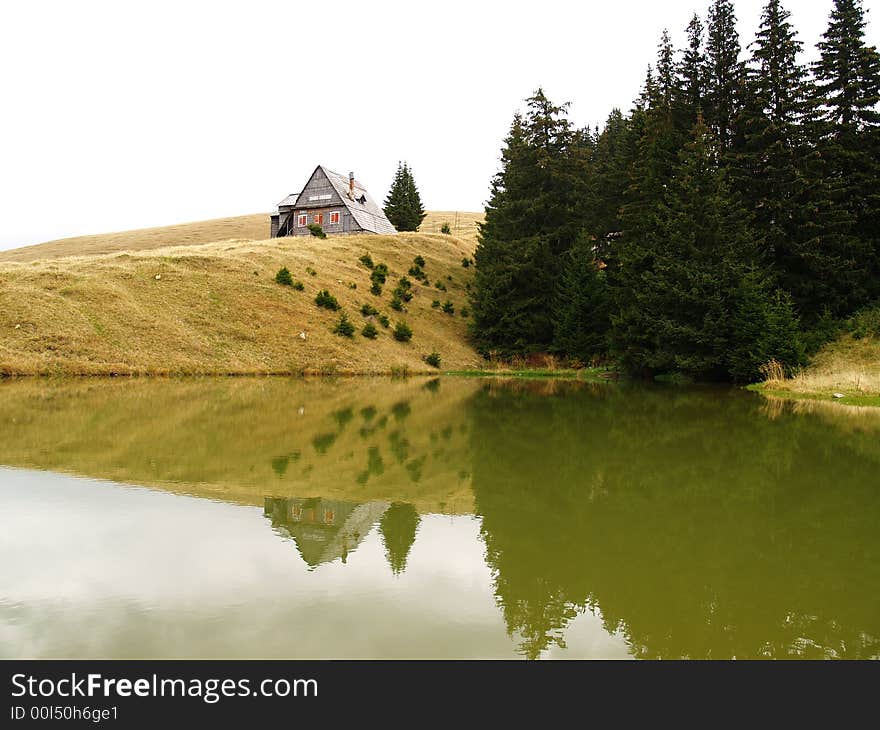 Trees reflecting into the lake water, with hut on the hill. Trees reflecting into the lake water, with hut on the hill