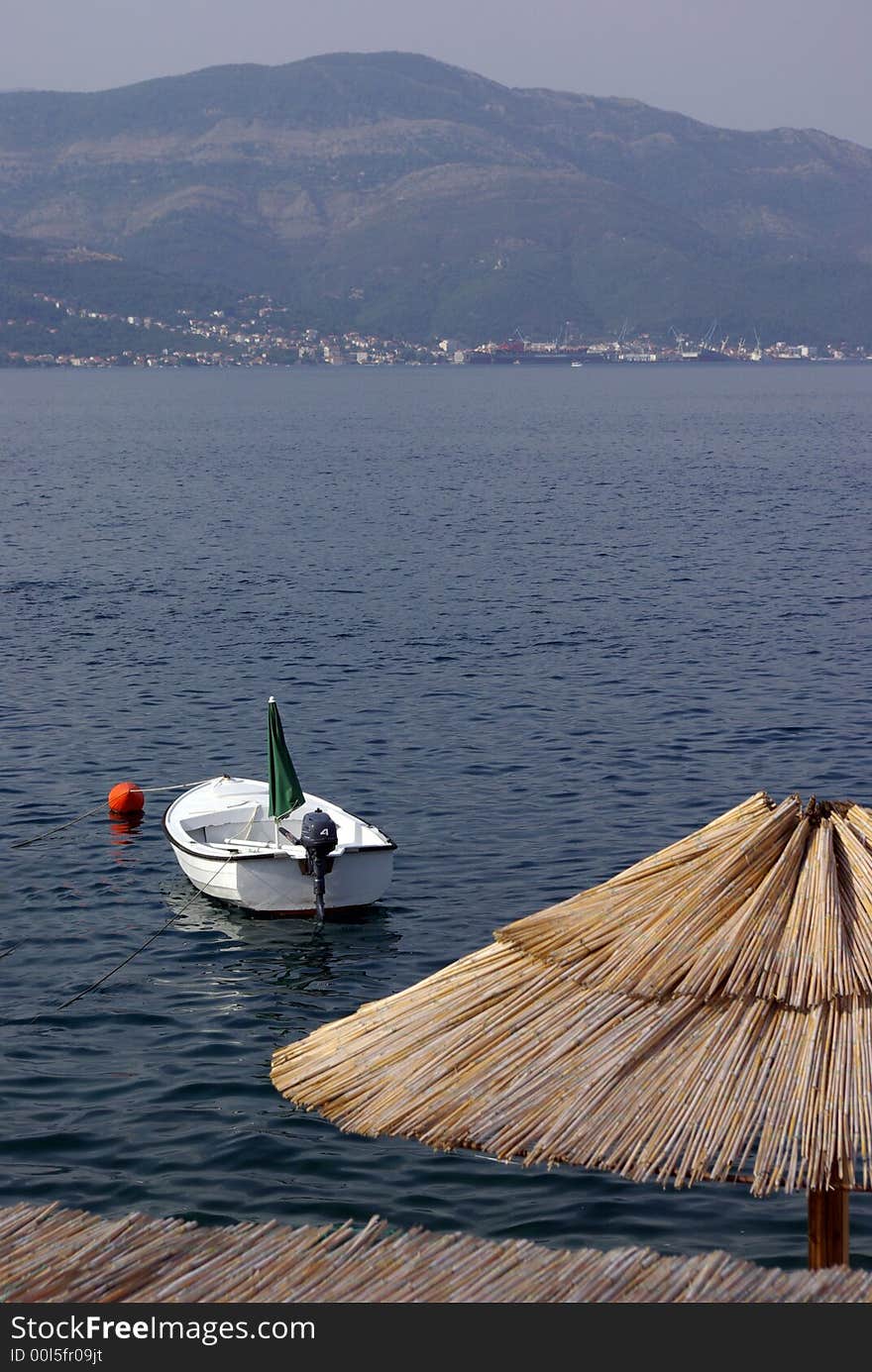 Shot from the terrace of the restaurant at the seaside showing sun umbrella with a boat and sea with mountains at the distance. Shot from the terrace of the restaurant at the seaside showing sun umbrella with a boat and sea with mountains at the distance