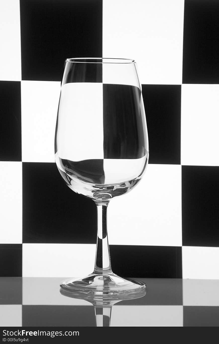 One glass on a checkered black-and-white background. Concept geometry still-life. One glass on a checkered black-and-white background. Concept geometry still-life.