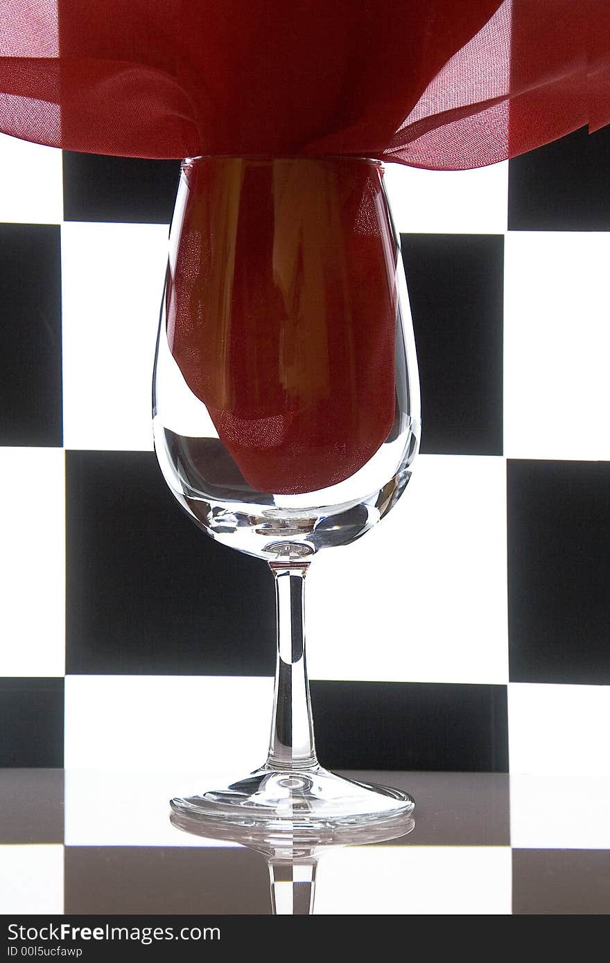 Glass and a red fabric on a checkered black-and-white background. Concept geometry still-life. Glass and a red fabric on a checkered black-and-white background. Concept geometry still-life.