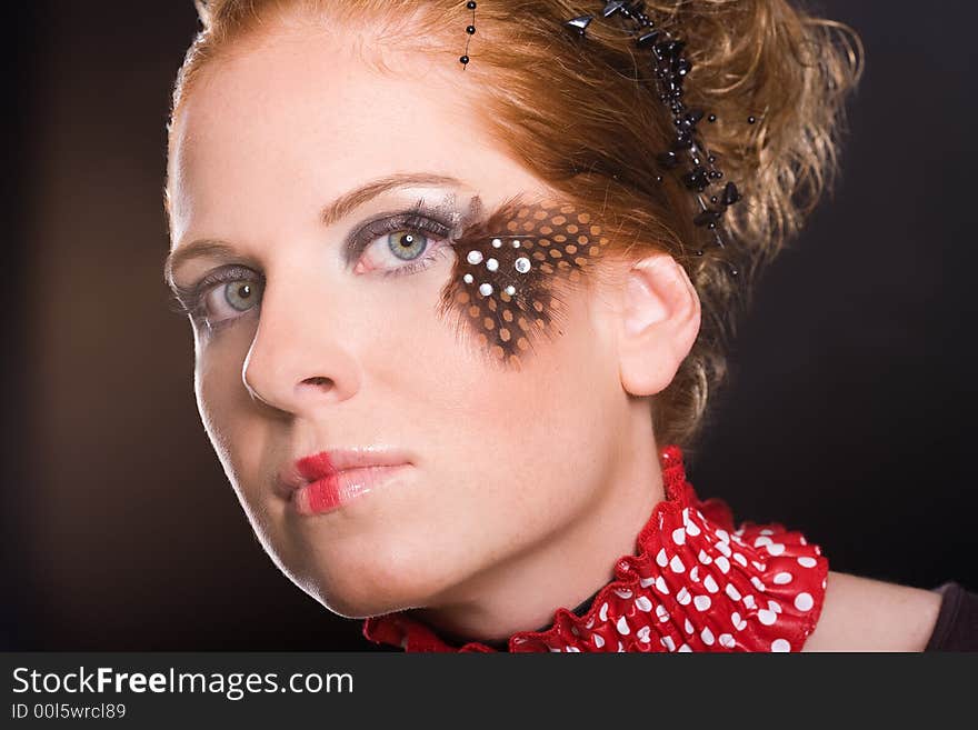 Attractive woman, unusual rogued, with feather on one eye and red-white vogue toby collar. Dark background. Attractive woman, unusual rogued, with feather on one eye and red-white vogue toby collar. Dark background.