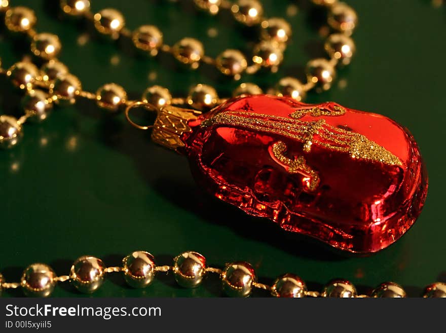 A piece of red and gold Christmas decoration shaped as a violin (cello, contrabass) with a string of gold beads, dark green background. A piece of red and gold Christmas decoration shaped as a violin (cello, contrabass) with a string of gold beads, dark green background.