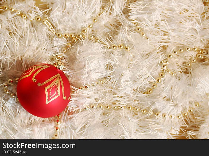 A red and gold piece of Christmas decoration lying in white and glittering strings and a string of gold beads. A red and gold piece of Christmas decoration lying in white and glittering strings and a string of gold beads.