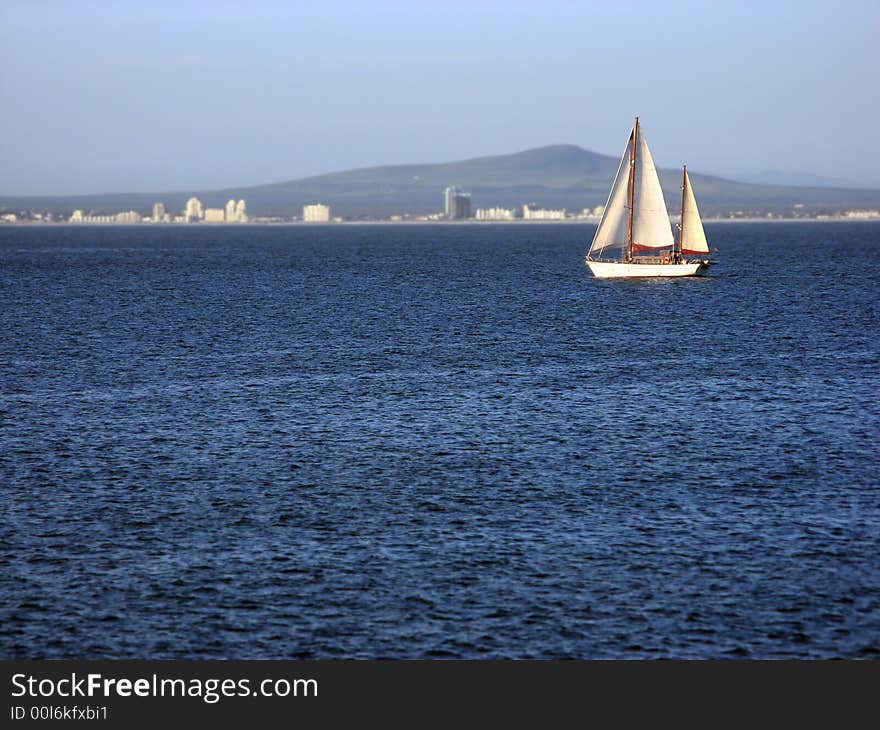 A single sailboat cruising across calm blue waters. A single sailboat cruising across calm blue waters