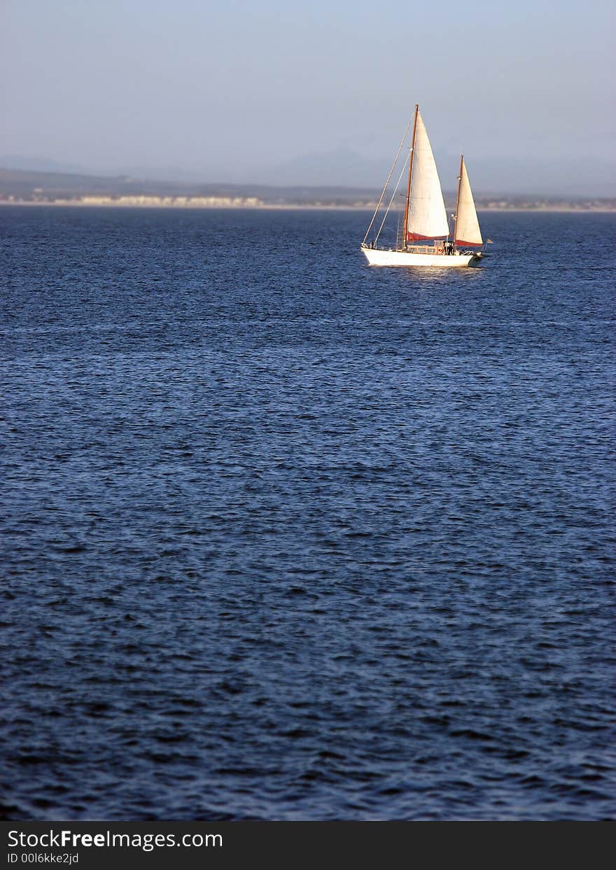 A single sailboat cruising across calm blue waters. A single sailboat cruising across calm blue waters