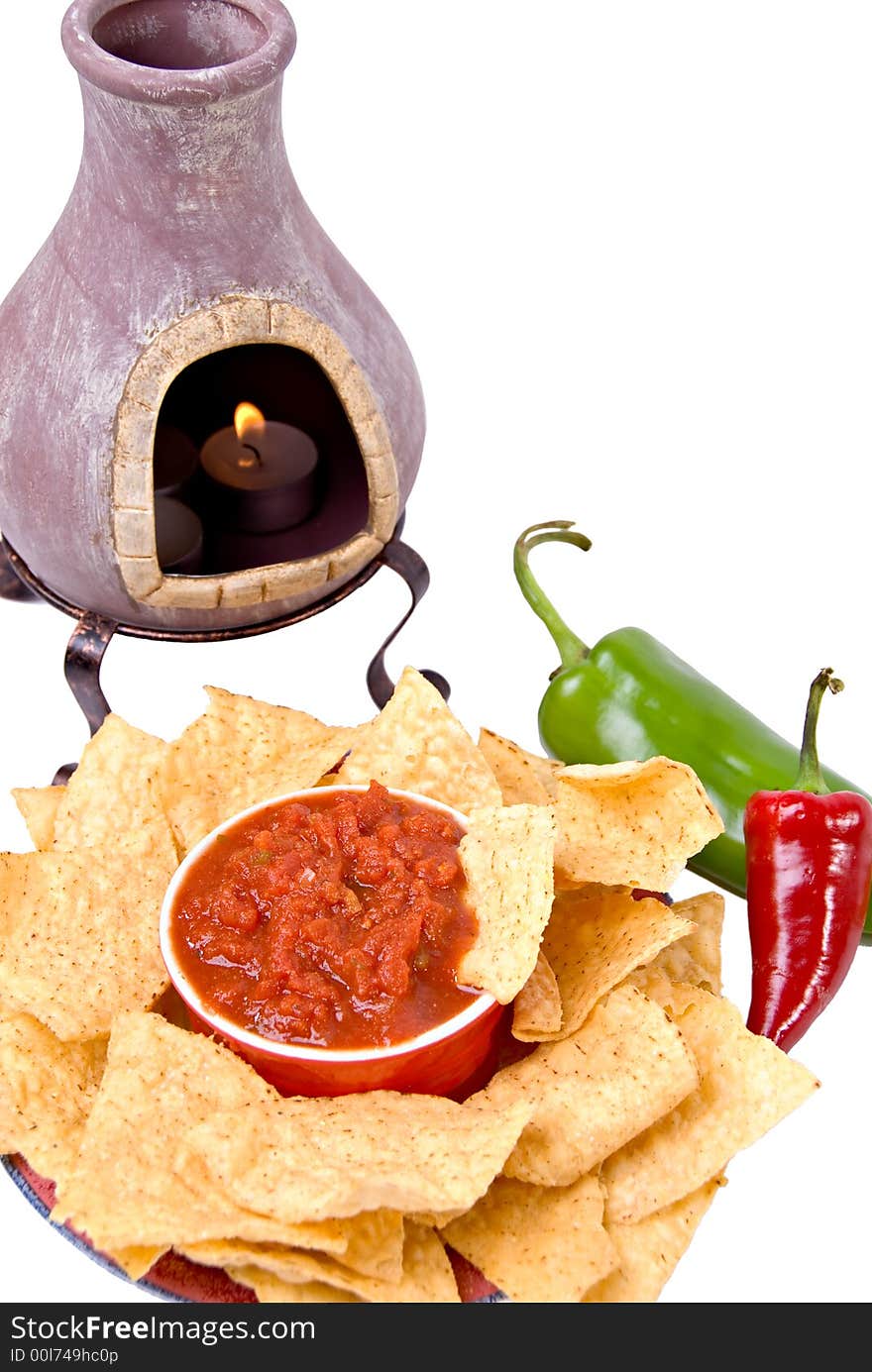 Mexican oven with lit candle next to plate and bowl of tortilla chips and salsa with anaheim and red jalapeno peppers. Mexican oven with lit candle next to plate and bowl of tortilla chips and salsa with anaheim and red jalapeno peppers