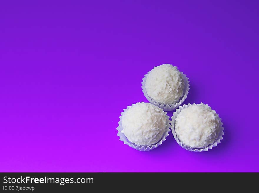 Appetizing candies with a nut and coconut are sparse on a violet background