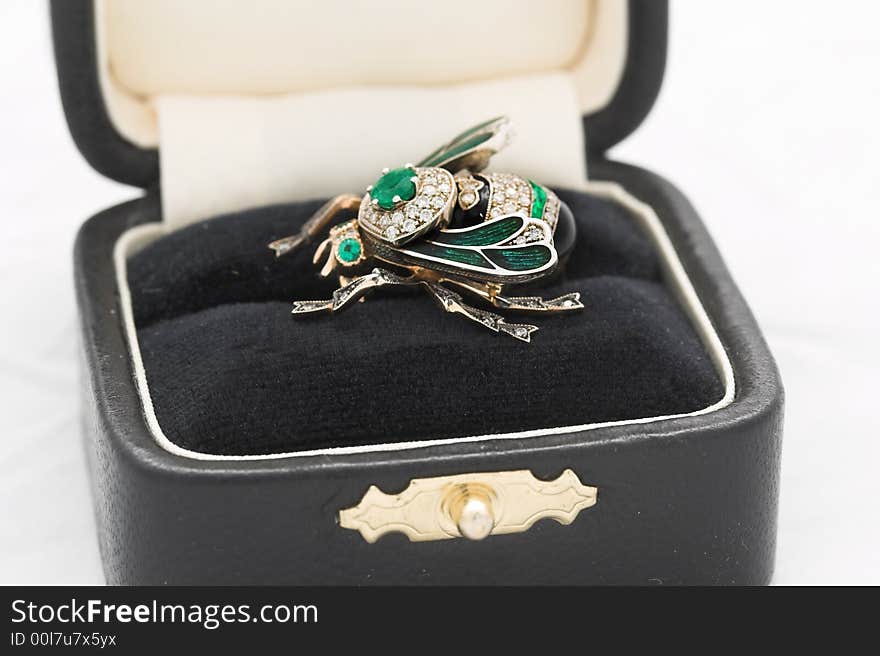 Jewelry from gold, emeralds, brilliants and platinum in the form of a bee in a small box on a white background. Jewelry from gold, emeralds, brilliants and platinum in the form of a bee in a small box on a white background