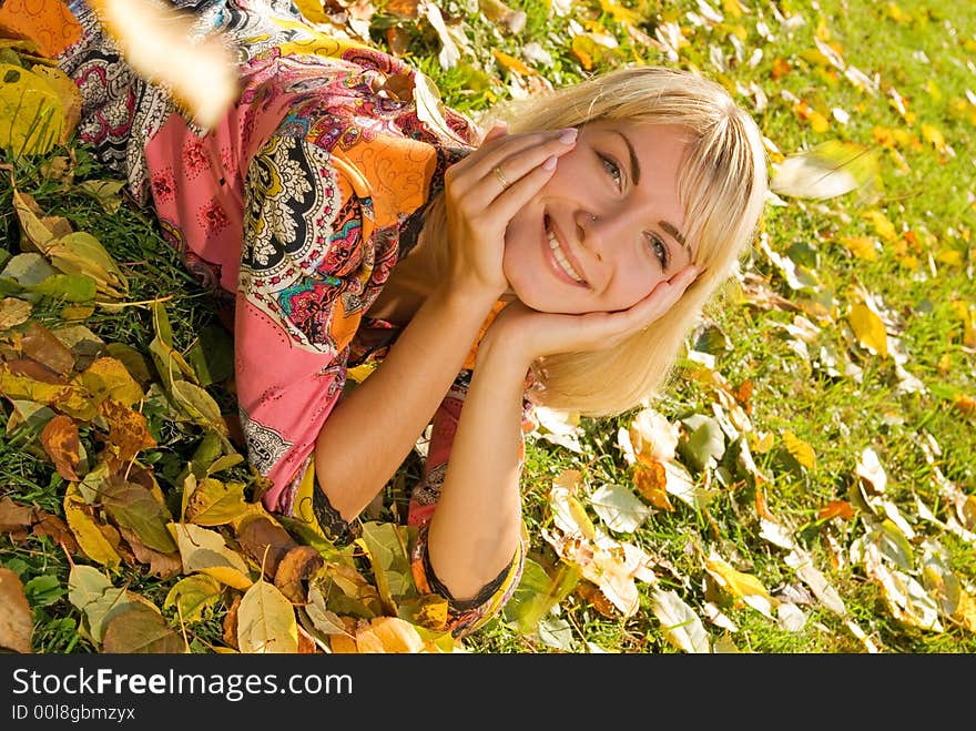 Blond cheerful girl lying on autumn leaves