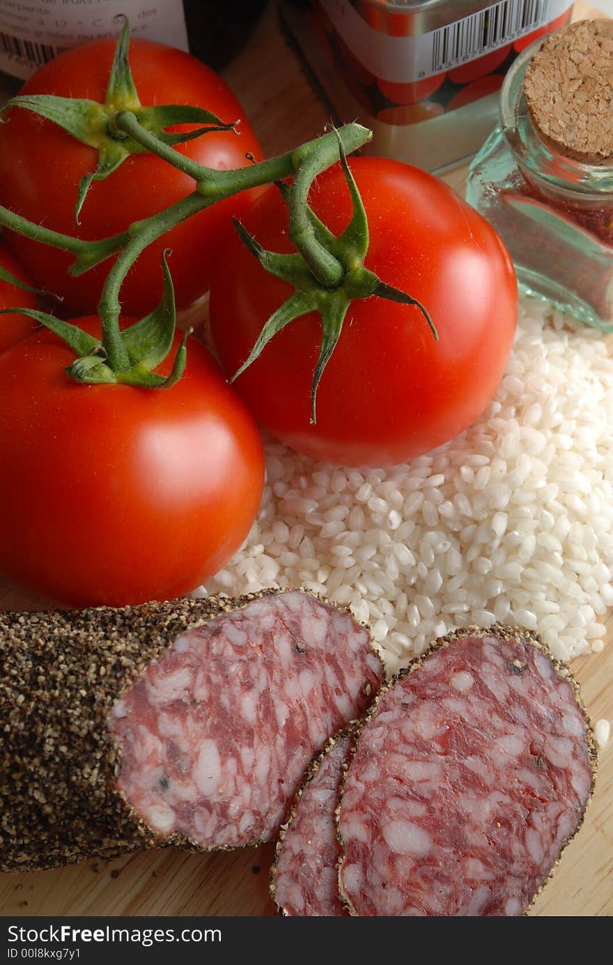 Piled up ingredients to make a risotto or paella, tin and jar of spices, tomatoes, rice and salami. Piled up ingredients to make a risotto or paella, tin and jar of spices, tomatoes, rice and salami