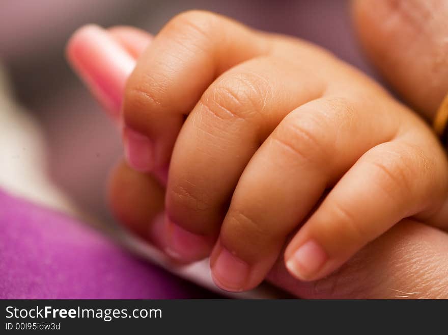 Tiny newborn baby fingers wrapped around adult female fingers up close. Tiny newborn baby fingers wrapped around adult female fingers up close