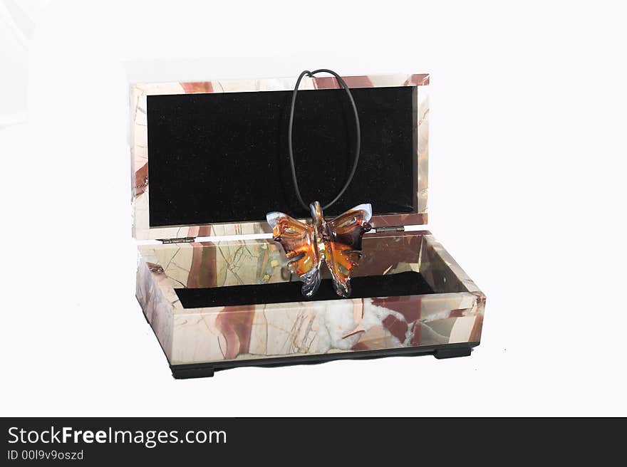 Casket from a color stone with an ornament in the form of the butterfly from multi-coloured glass on a black leather cord on a white background. Casket from a color stone with an ornament in the form of the butterfly from multi-coloured glass on a black leather cord on a white background